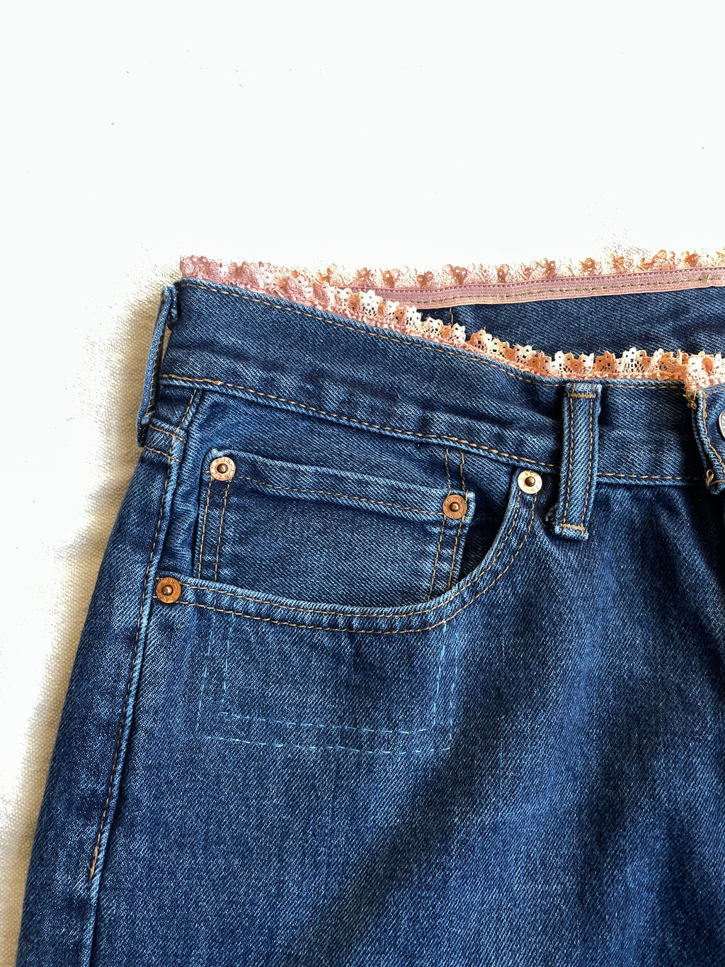 Close-up of blue denim jeans with lace trim on a white background