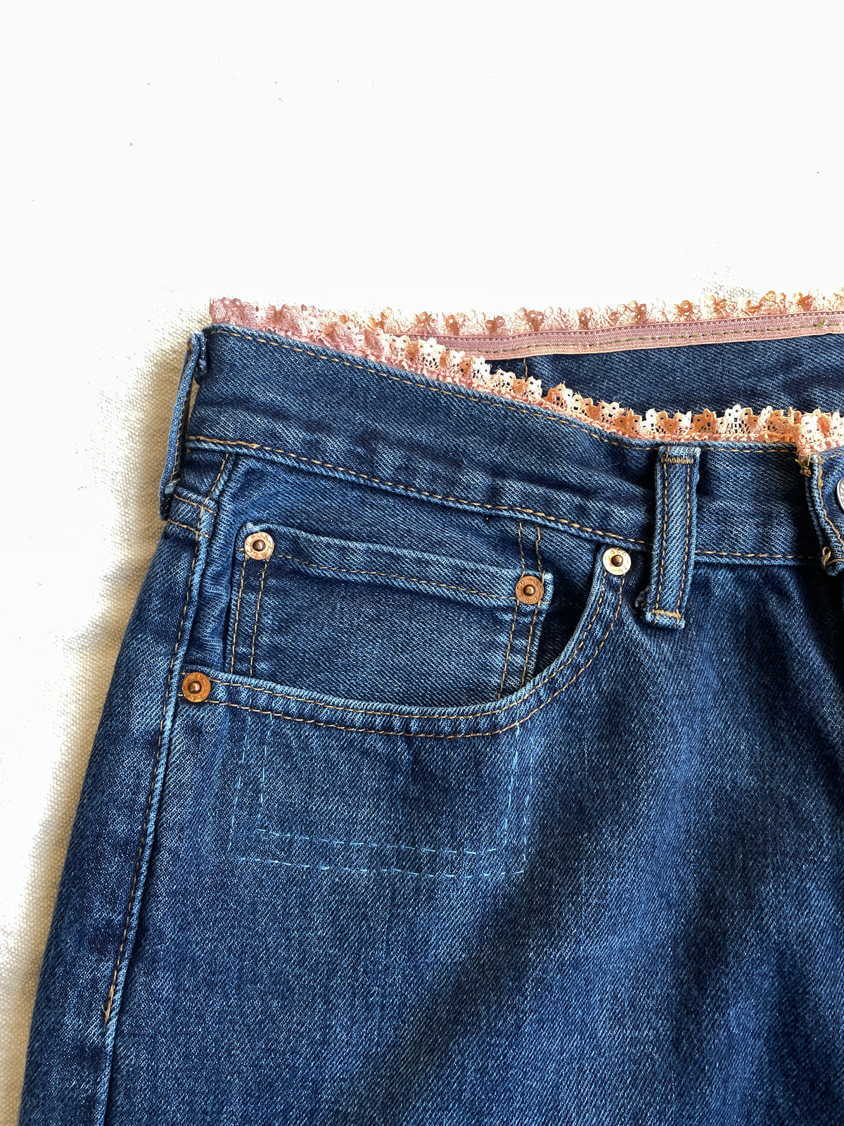 Close-up of blue denim jeans with lace trim on a white background