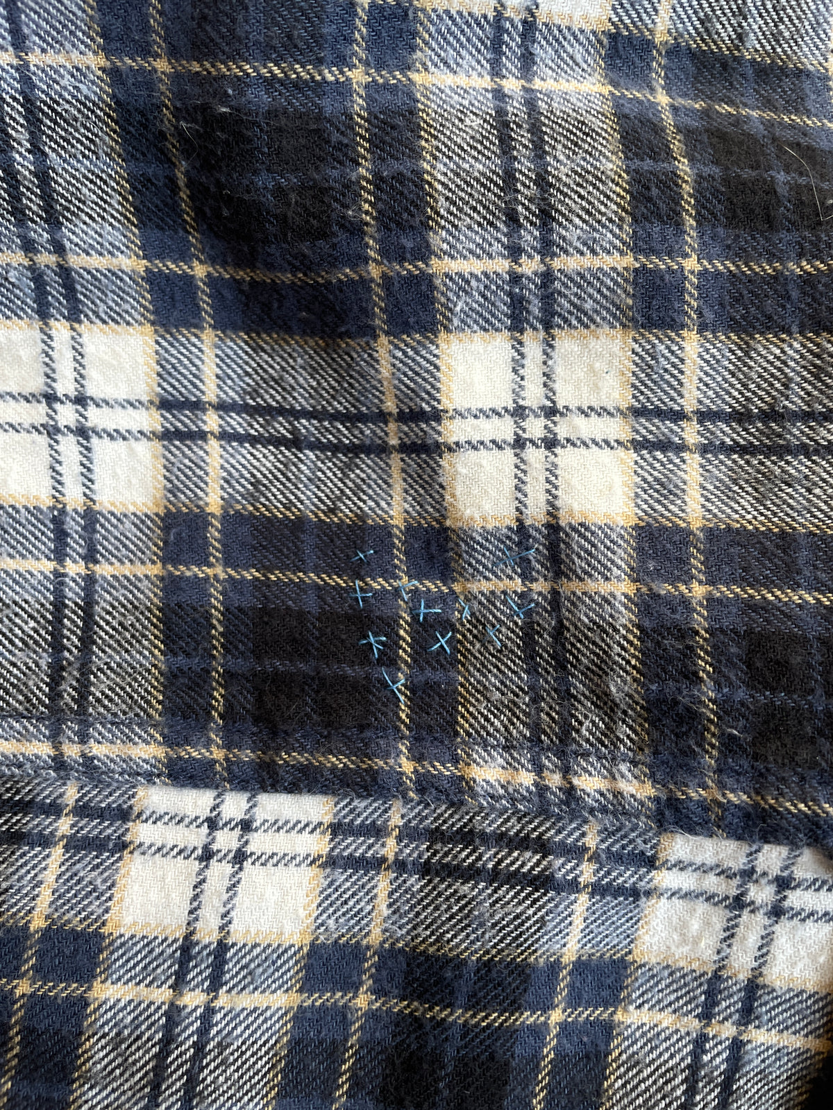 Close-up of blue hand stitch on plaid flannel